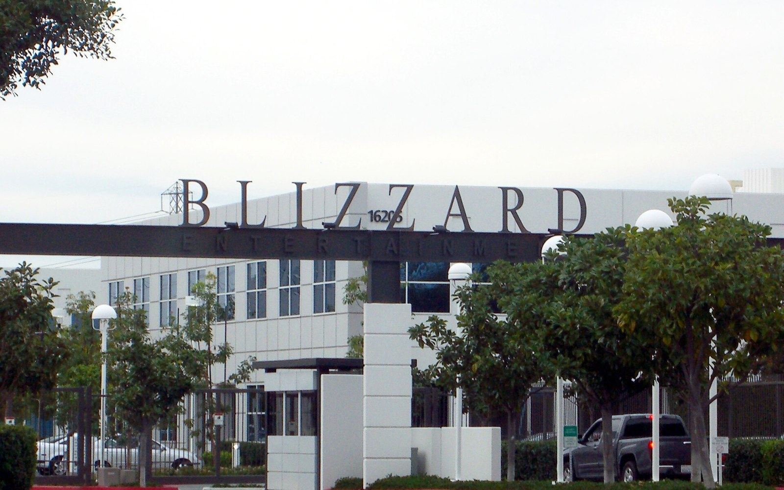 Blizzard Entertainment's office building sign above trees and a parking lot entrance