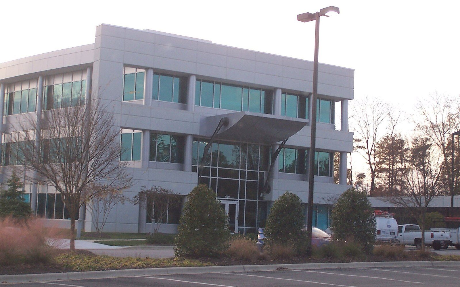 Three-story glass and metal office building with a canopied entrance and parking lot