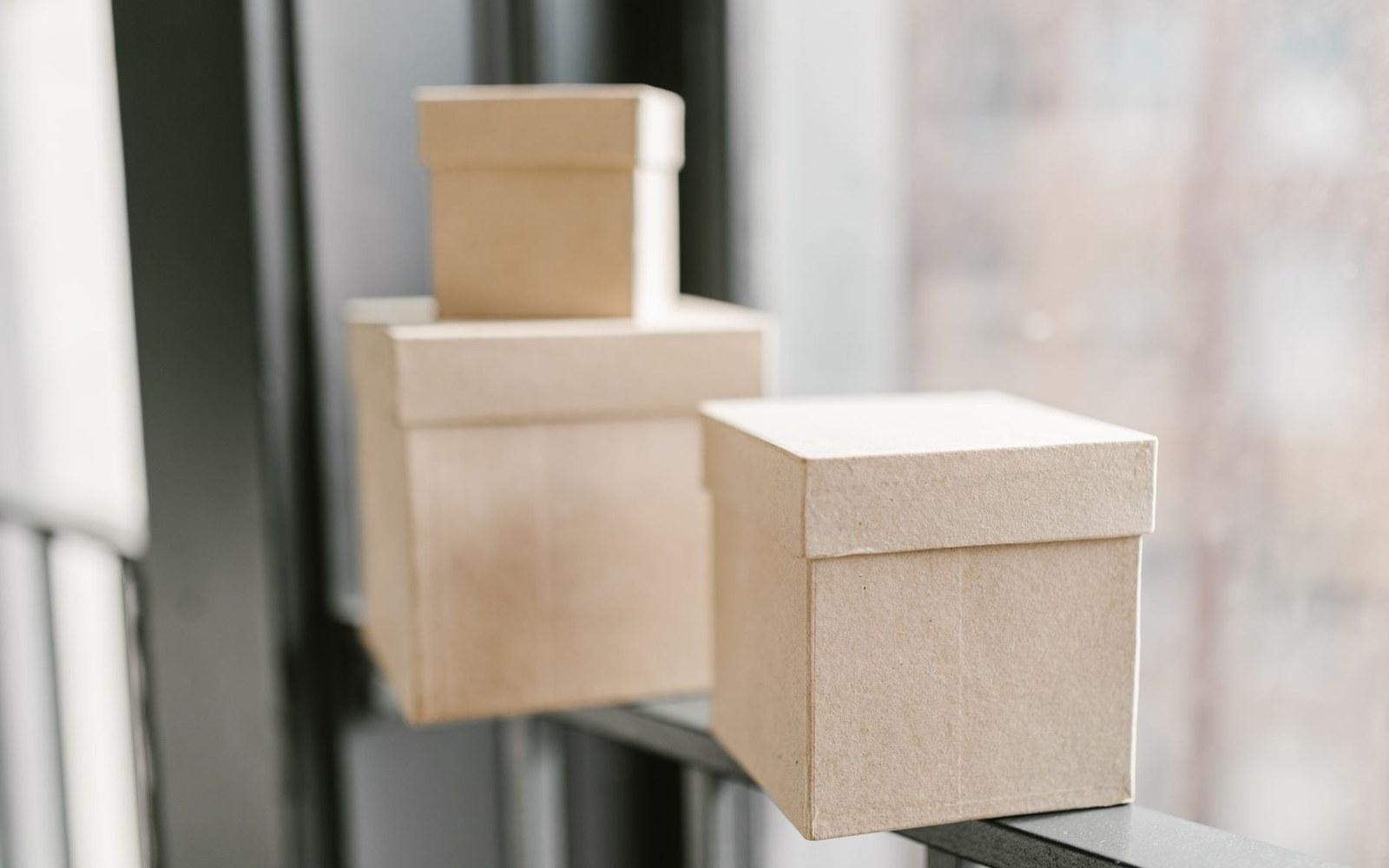 Small cardboard boxes with lids stacked on a windowsill railing
