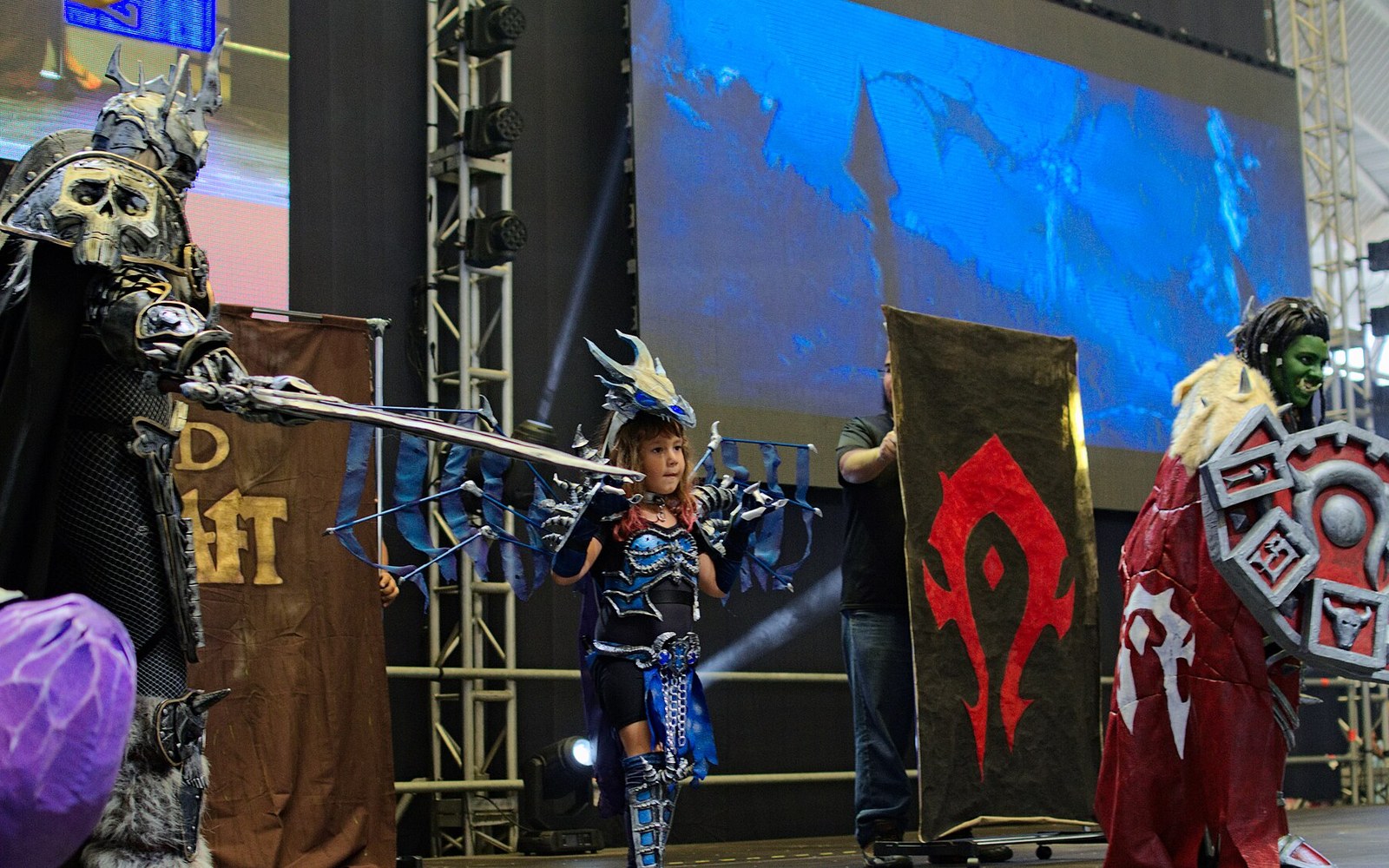 Cosplayers in armored costumes stand on stage beside a red Horde banner from World of Warcraft