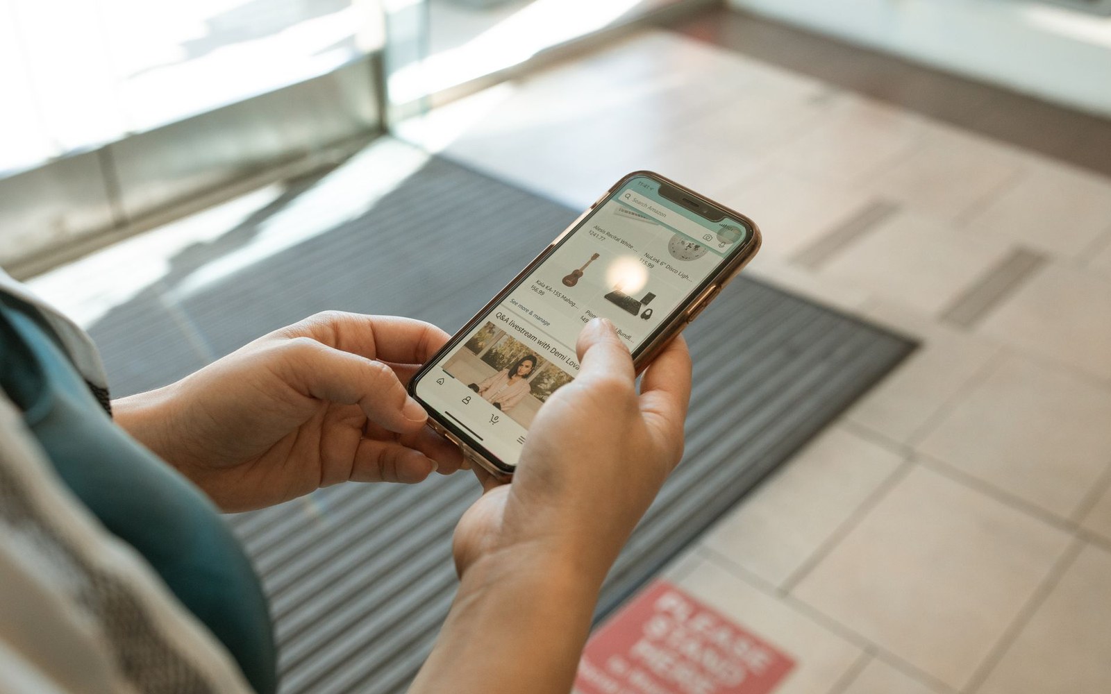 An adult hand holding a phone showing a mobile MMO's in-game store screen, background out of focus